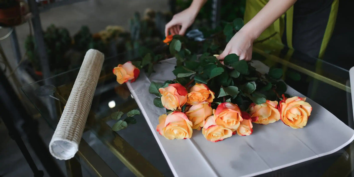 Florist lägger orange rosor på papper för att binda en bukett vid en arbetsbänk i en blomsterbutik.