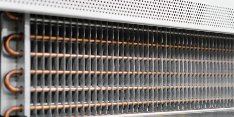 Närbild på en förångare med tunna aluminiumlameller och kopparrör bakom en perforerad panel i en kyl