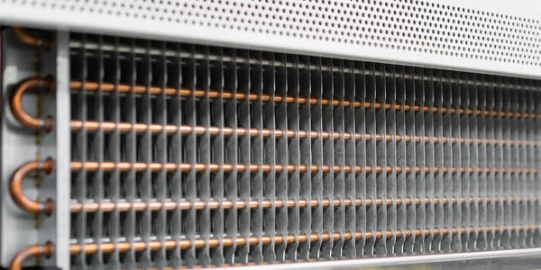Närbild på en förångare med tunna aluminiumlameller och kopparrör bakom en perforerad panel i en kyl