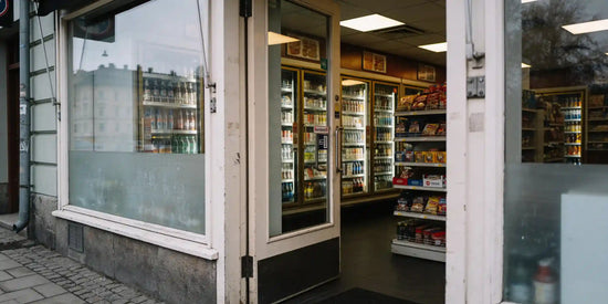 Öppen dörr in till en kiosk i Stockholm med kylskåp och snackshyllor