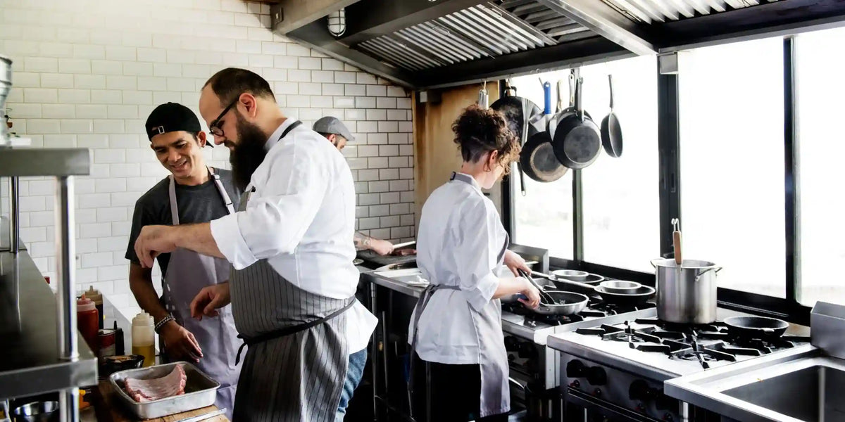 Kockar samarbetar i ett restaurangkök medan de förbereder mat vid spisen.