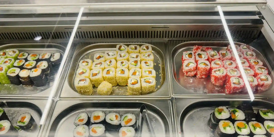 Sushivitrin uppifrån med makirullar i rostfria GN-lådor, bakom glas