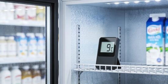 Digital termometer som visar 9 °C på en hylla i en butikskyl med öppen glasdörr och mjölkpaket i bakgrunden.
